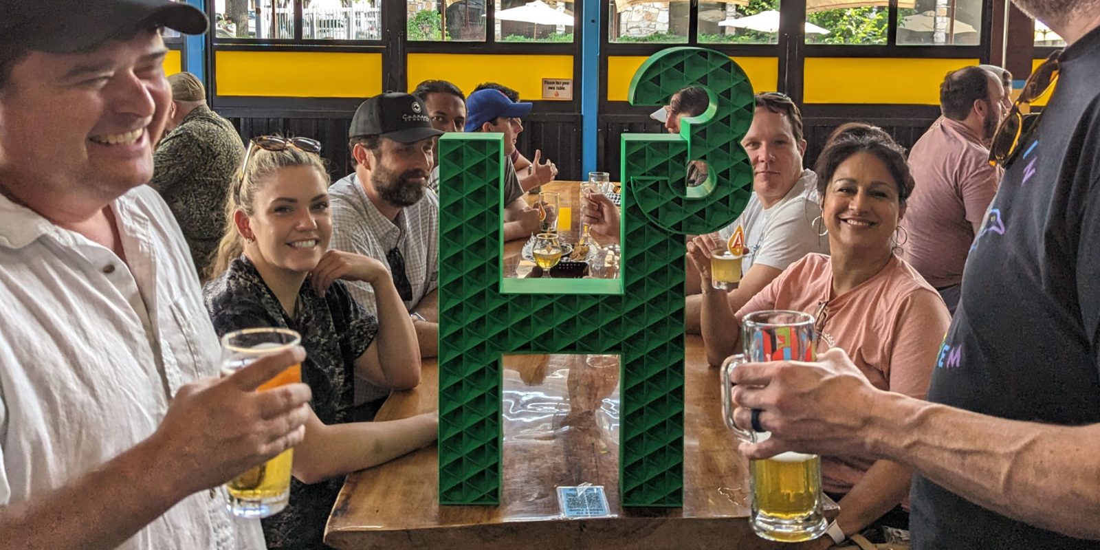 Attendees at an H³ ATX happy hour posing with the H³ sign